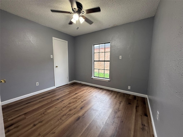 empty room featuring ceiling fan, a textured ceiling, baseboards, and dark wood-type flooring
