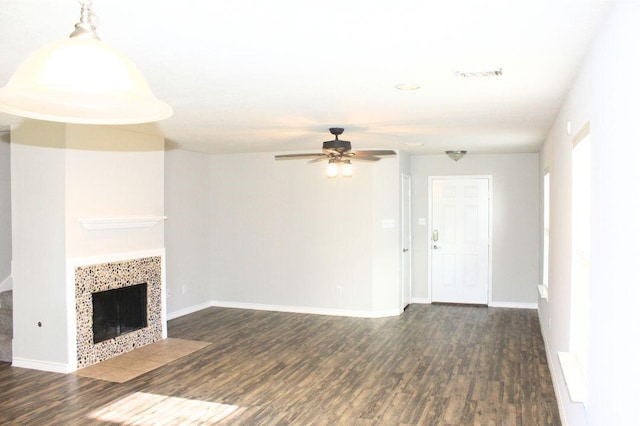 unfurnished living room featuring ceiling fan, dark wood-type flooring, a tile fireplace, and baseboards
