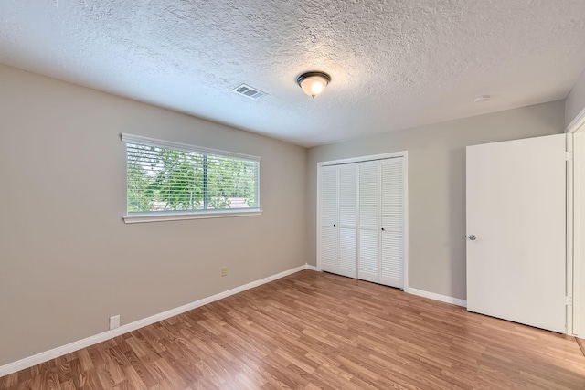 unfurnished bedroom featuring light wood-style flooring, a closet, a textured ceiling, visible vents, and baseboards