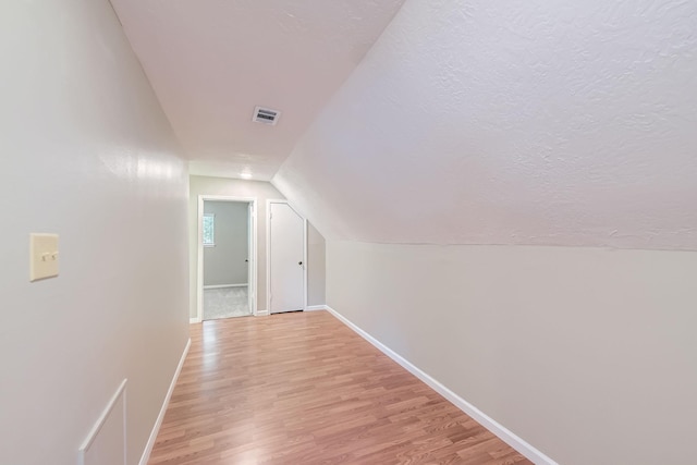 bonus room featuring a textured ceiling, visible vents, vaulted ceiling, light wood-style flooring, and baseboards