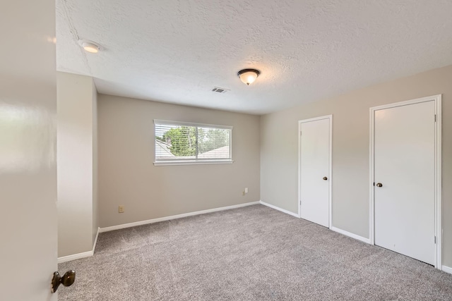 unfurnished bedroom with a textured ceiling, carpet floors, baseboards, and visible vents
