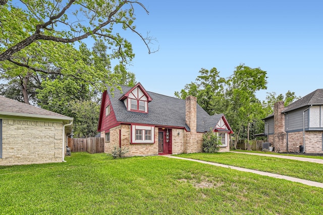 english style home with brick siding, a chimney, fence, and a front yard