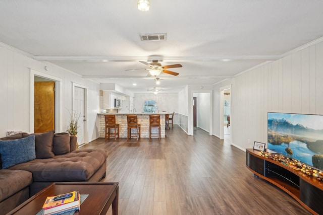living area featuring dark wood finished floors, visible vents, a ceiling fan, and ornamental molding