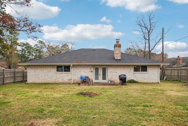 rear view of house featuring french doors, a chimney, a lawn, and a fenced backyard