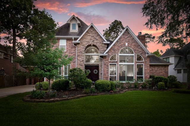 view of front of house with a yard, a chimney, brick siding, and driveway