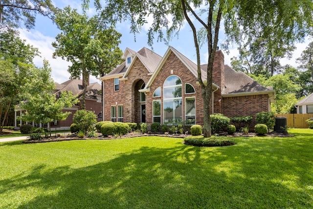 traditional home with central AC, a chimney, fence, a front yard, and brick siding