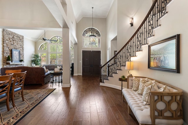 foyer entrance with ceiling fan with notable chandelier, high vaulted ceiling, dark wood-type flooring, baseboards, and stairs