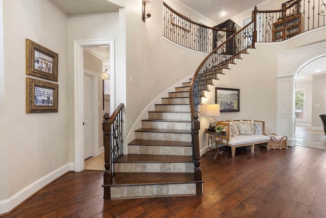 staircase featuring baseboards, wood-type flooring, crown molding, and a high ceiling