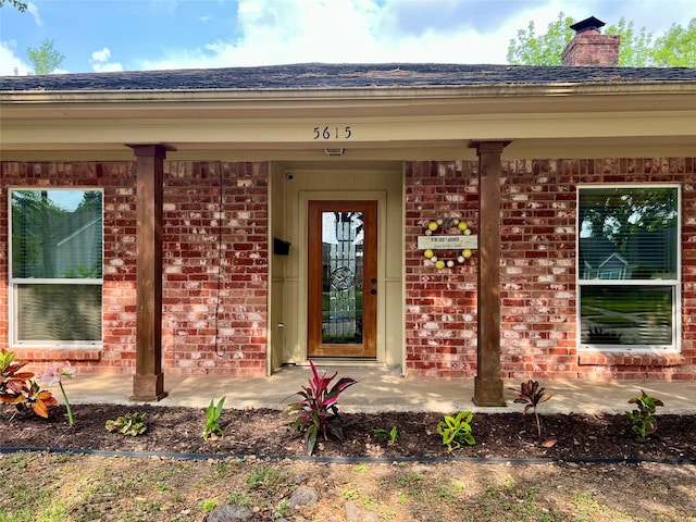 property entrance featuring brick siding, roof with shingles, a chimney, and a porch