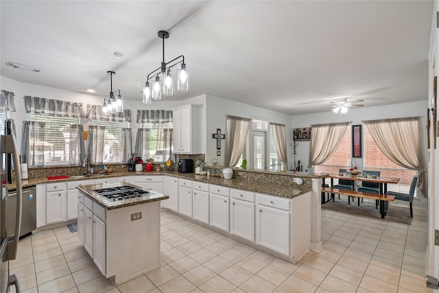kitchen with light tile patterned floors, a peninsula, appliances with stainless steel finishes, and a sink
