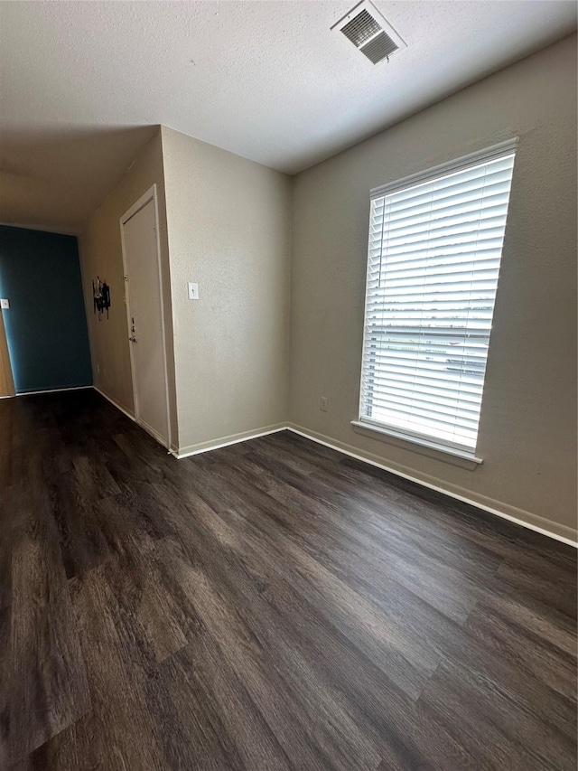 unfurnished room with baseboards, visible vents, and dark wood finished floors