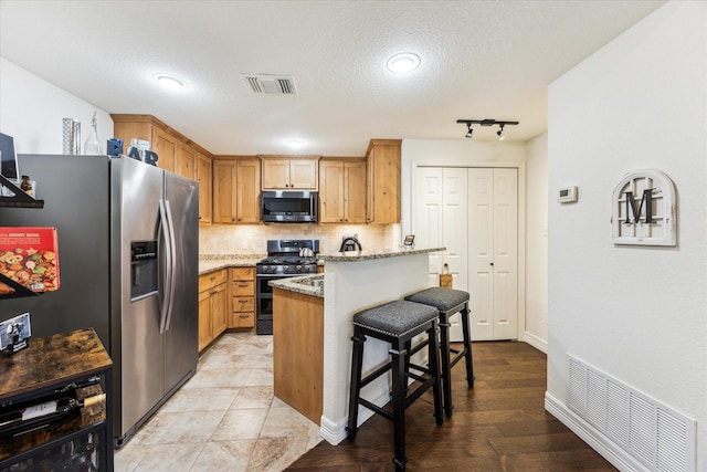 1210 Persimmon Pass, Fischer, TX 78623 - kitchen featuring appliances with stainless steel finishes, a breakfast bar area, decorative backsplash, light stone counters, and a textured ceiling