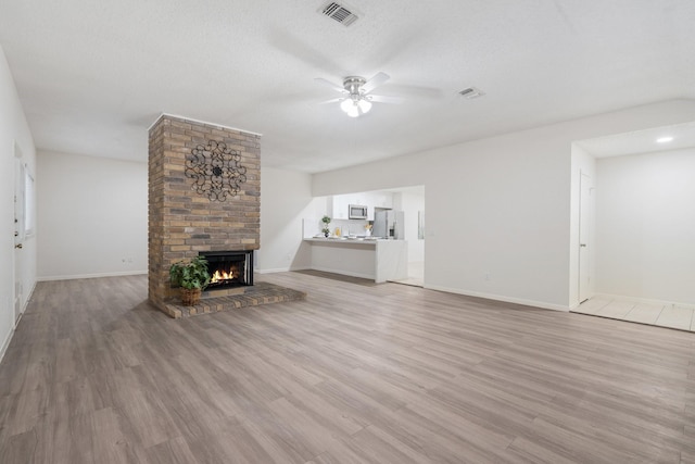 34 Quiet Peace Pl, The Woodlands, TX 77381 - unfurnished living room with a ceiling fan, a brick fireplace, light wood-style floors, baseboards, and a textured ceiling