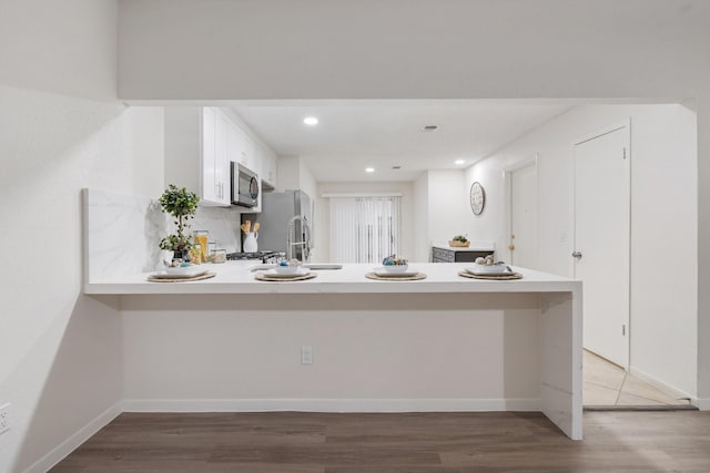 34 Quiet Peace Pl, The Woodlands, TX 77381 - kitchen with stainless steel appliances, a peninsula, light countertops, light wood-type flooring, and white cabinets