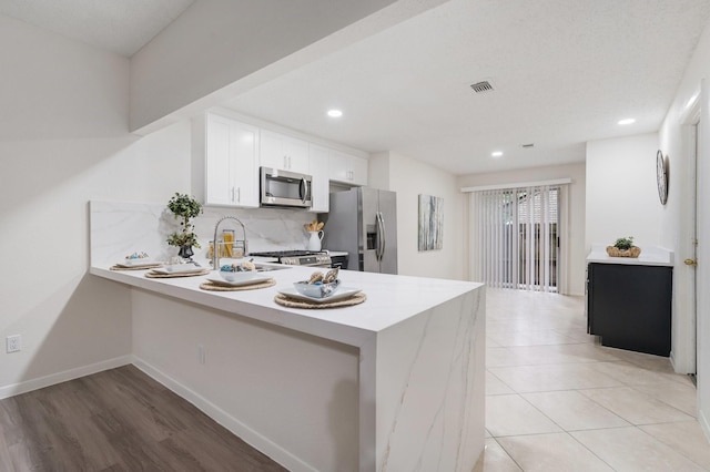 34 Quiet Peace Pl, The Woodlands, TX 77381 - kitchen with stainless steel appliances, backsplash, light countertops, a peninsula, and white cabinets