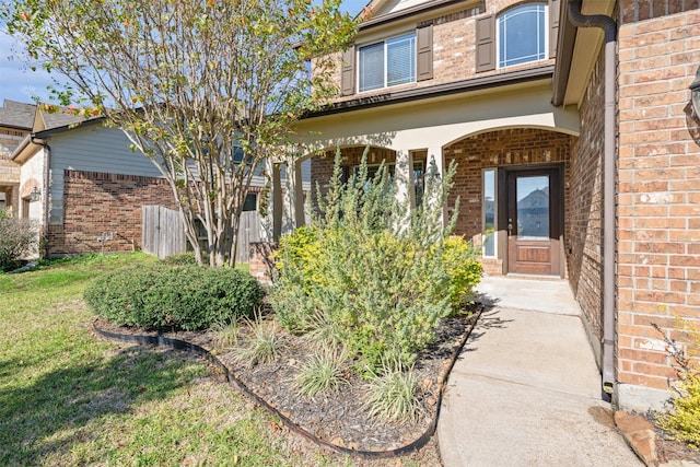 doorway to property with brick siding, a lawn, and covered porch