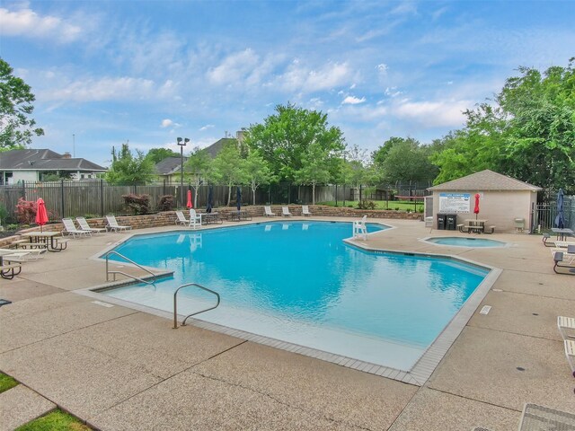 community pool with fence, a patio area, and a hot tub