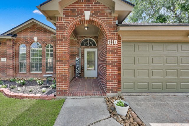 doorway to property featuring brick siding, an attached garage, and concrete driveway