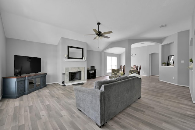 living area featuring vaulted ceiling, arched walkways, light wood-style floors, a ceiling fan, and a fireplace