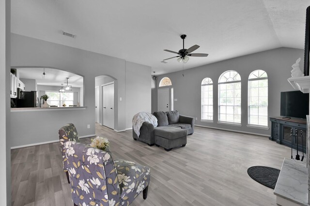 living area featuring arched walkways, a ceiling fan, plenty of natural light, wood finished floors, and vaulted ceiling