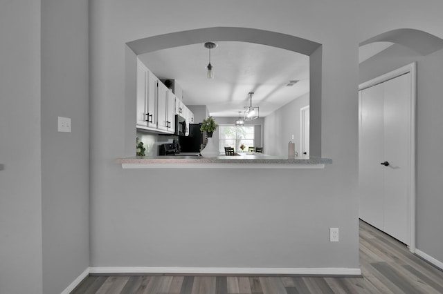 kitchen featuring arched walkways, wood finished floors, light countertops, white cabinetry, and baseboards