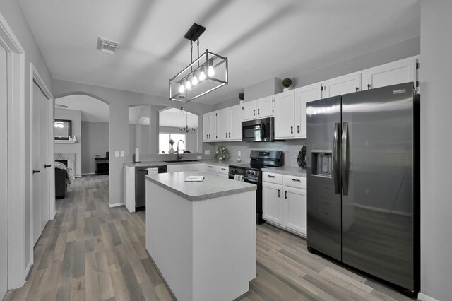 kitchen featuring appliances with stainless steel finishes, arched walkways, a sink, light countertops, and white cabinets
