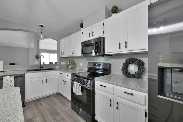 kitchen featuring stainless steel appliances, a sink, light countertops, white cabinetry, and arched walkways