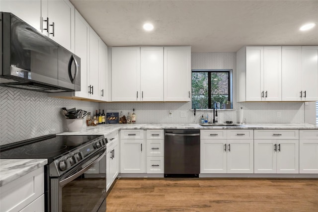 kitchen featuring stainless steel dishwasher, electric range oven, a sink, light wood-type flooring, and decorative backsplash