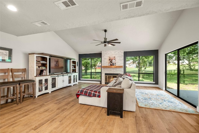 living room with wood finished floors, a ceiling fan, a textured ceiling, high vaulted ceiling, and a stone fireplace