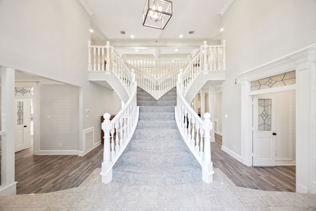 staircase with wood finished floors, a high ceiling, a chandelier, baseboards, and crown molding