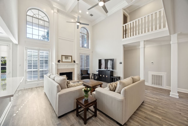 living room featuring a towering ceiling, decorative columns, ceiling fan, a fireplace, and beamed ceiling
