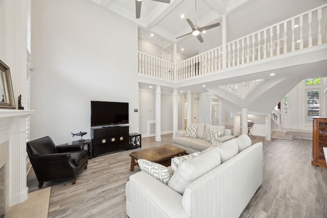 living area with a ceiling fan, a towering ceiling, light wood-style flooring, beam ceiling, and ornate columns