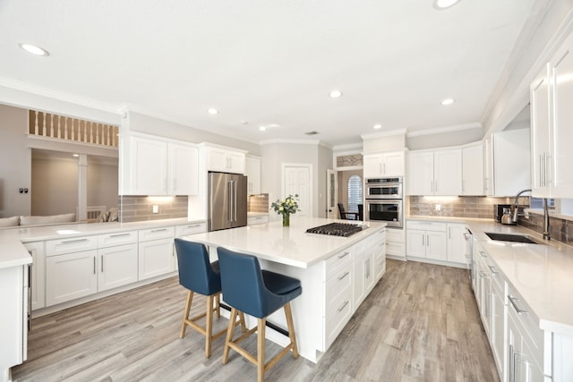 kitchen featuring appliances with stainless steel finishes, a sink, a center island, backsplash, and light wood-style flooring