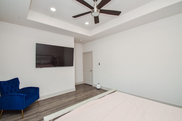 bedroom with wood finished floors, recessed lighting, a tray ceiling, baseboards, and ceiling fan