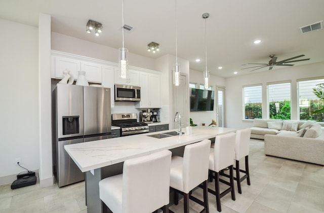 kitchen with appliances with stainless steel finishes, a sink, a kitchen island with sink, a breakfast bar area, and recessed lighting