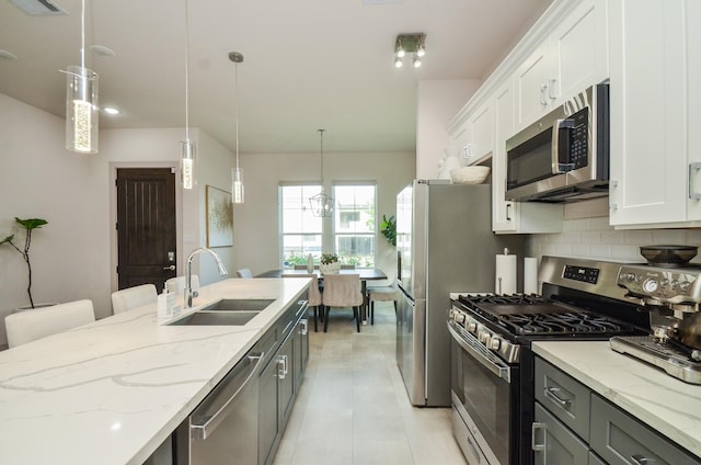kitchen with stainless steel appliances, a sink, backsplash, light stone counters, and white cabinetry
