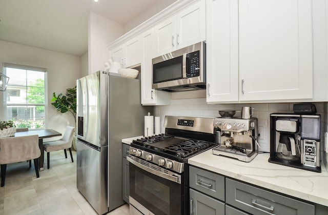 kitchen featuring stainless steel appliances, gray cabinets, tasteful backsplash, light stone countertops, and white cabinetry