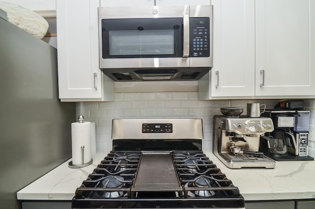 kitchen with appliances with stainless steel finishes, tasteful backsplash, white cabinets, and light stone countertops