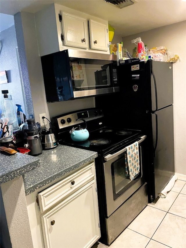 kitchen featuring stainless steel appliances, light tile patterned floors, white cabinets, and dark countertops