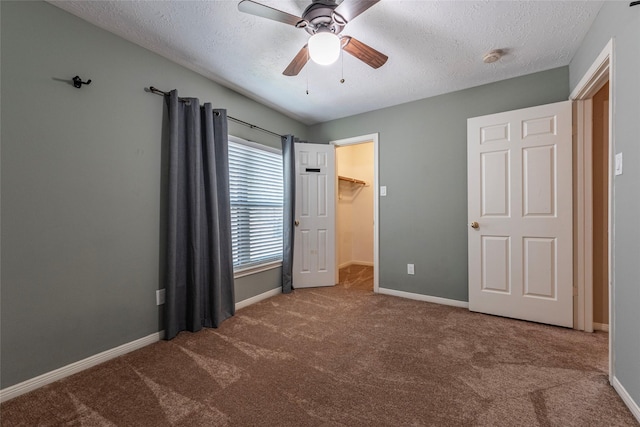 unfurnished bedroom with a textured ceiling, carpet flooring, baseboards, a spacious closet, and a ceiling fan