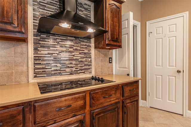 kitchen featuring wall chimney exhaust hood, black electric cooktop, backsplash, light countertops, and light tile patterned flooring