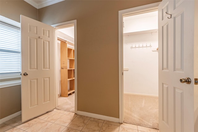 hallway featuring ornamental molding, light carpet, baseboards, and light tile patterned floors