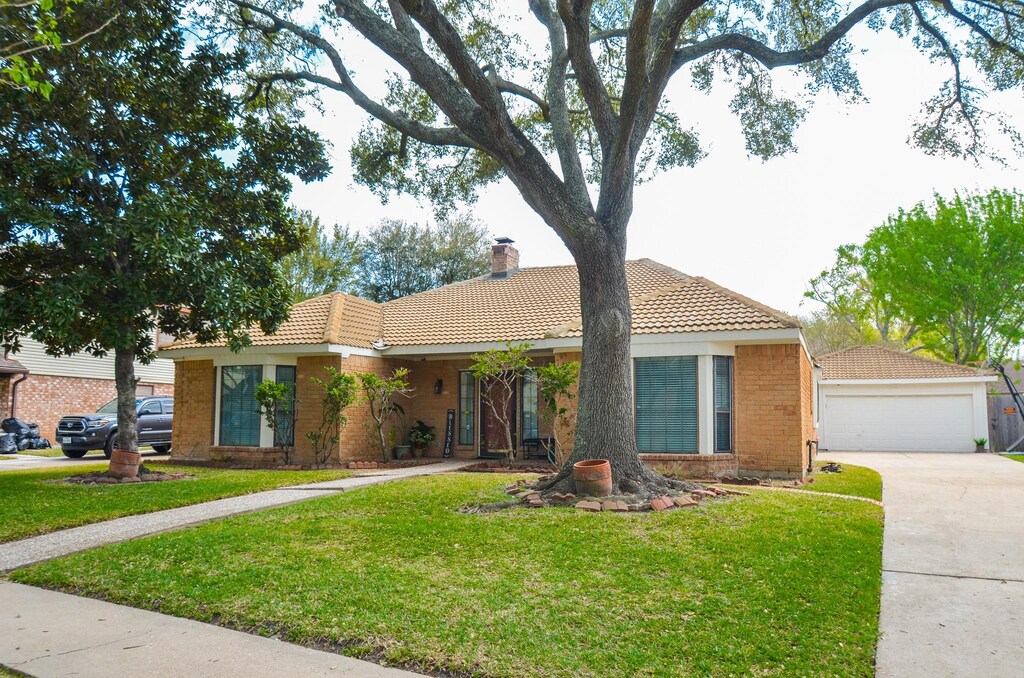 single story home with a tiled roof, a chimney, a front lawn, brick siding, and a detached garage