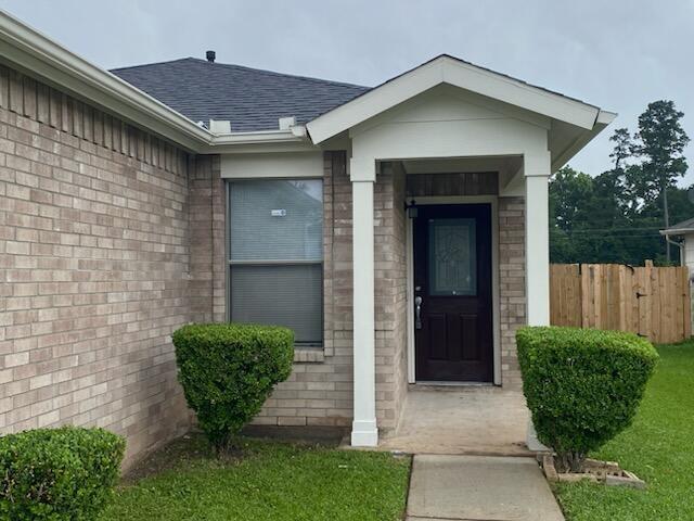 doorway to property featuring brick siding and roof with shingles