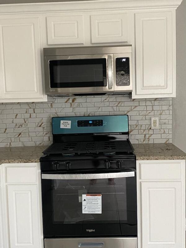kitchen with appliances with stainless steel finishes, tasteful backsplash, white cabinets, and light stone countertops