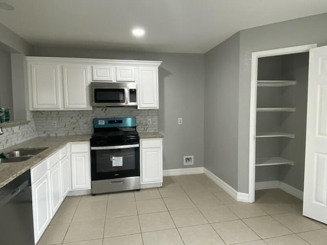 kitchen featuring appliances with stainless steel finishes, backsplash, a sink, white cabinets, and light tile patterned floors