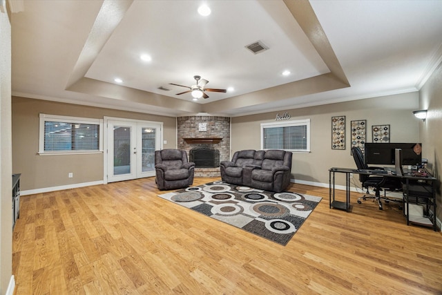 living room with a tray ceiling, a ceiling fan, a brick fireplace, baseboards, and crown molding