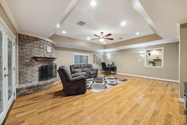 living area featuring ornamental molding, a raised ceiling, wood finished floors, a fireplace, and a ceiling fan