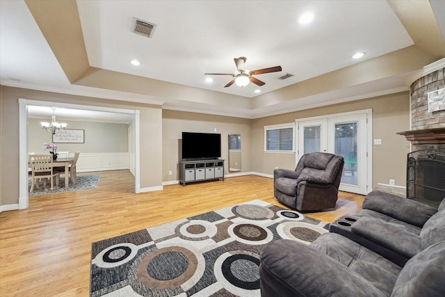 living area featuring light wood finished floors, a chandelier, a ceiling fan, a fireplace, and ornamental molding