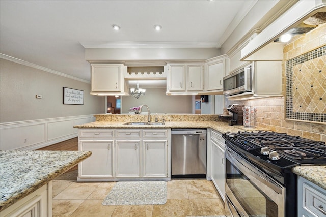 kitchen featuring appliances with stainless steel finishes, a sink, ornamental molding, a peninsula, and light stone counters